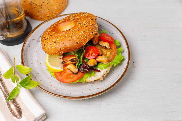 bagel with salad, mussels and cream cheese. On a light wooden table, set for breakfast or lunch. Horizontal, copy of the space stock photo