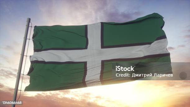 Devon Flag England Waving In The Wind Sky And Sun Background 3d Rendering Stock Photo - Download Image Now