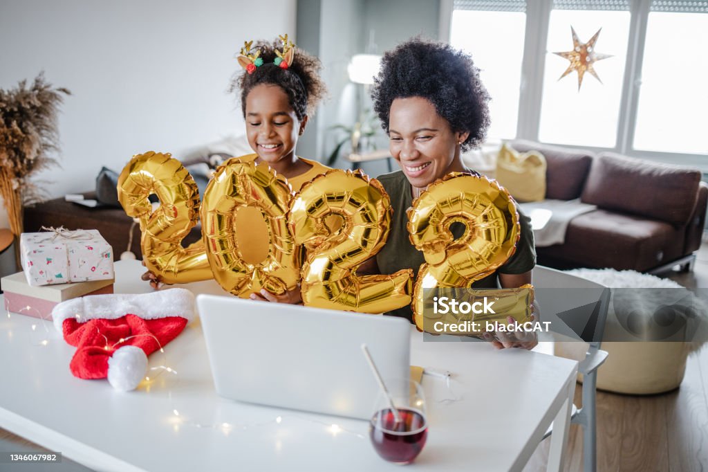 Mother and daughter celebrating online 2022. year and holding balloons Mother and daughter are at home, they are holding 2020. balloon numbers and communicating on a video call New Year Resolution Stock Photo