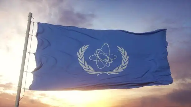 Flag of International Atomic Energy Agency IAEA waving in the wind, sky and sun background. 3d rendering.