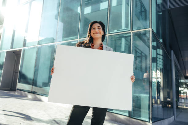 activista empresarial sosteniendo una pancarta en blanco fuera de su lugar de trabajo - businesswoman advertise placard advertisement fotografías e imágenes de stock