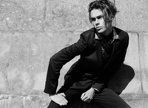 Portrait of sexy handsome fashion nale model dressed in elegant suit posing outdoor. Long haired Metrosexual. Black and white picture.