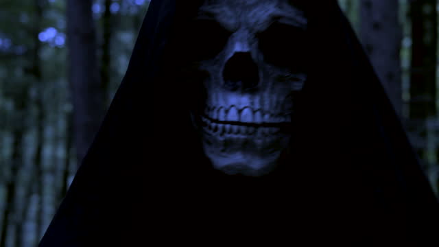 Grim Reaper skull walking to the camera in the woods in the dark.