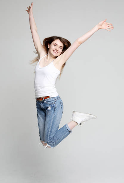istock smiling young woman jumping in air over white background 1346087329
