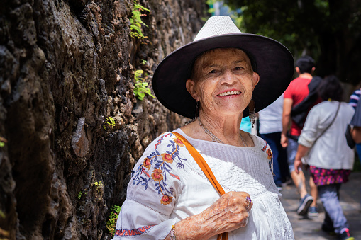 adult Latina woman, smiling at the camera. She walks along a stone path.