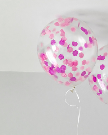 Helium filled balloons near a ceiling. Transparent and with pink and purple confetti. Birthday celebration concept for girls.