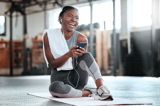 Shot of a young beautiful woman using her cellphone and earphones after her workout at the gym