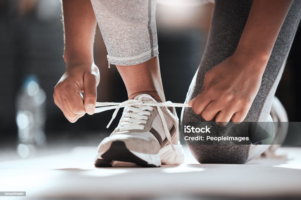 Cropped shot of an unrecognizable woman tying her shoelaces while exercising at the gym Should come with a warning Sports Shoe Stock Photo