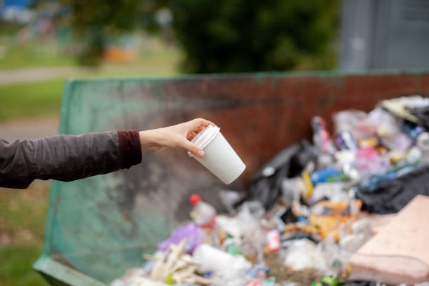 istock Woman throwing a cardboard glass into a recycling bin. large trash bin 1346096630