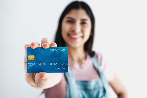 Young hispanic woman holding blue credit card isolated over white background in Latin America