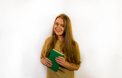 Front view of aged 20-29 years old who is beautiful caucasian female university student standing in front of white background who is studying and holding textbook