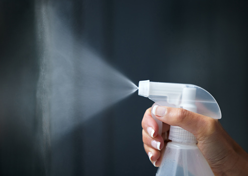 Image with human hand holding a spray container and spraying