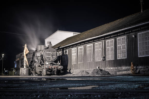 Old steam locomotive being fired up in front of a shed during the night. Romantic photo of a steam engine during the night. Vertical photo