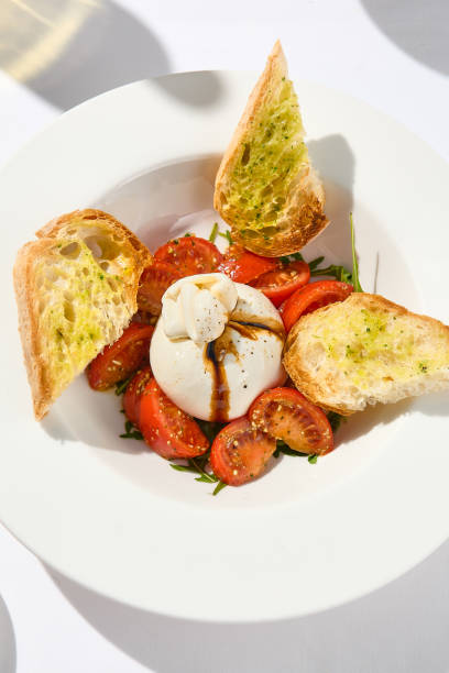 salade italienne traditionnelle avec fromage burrata et tomates. caprese fantaisie avec fromage burrata, tomates cerises, pesto et sauces balsamiques. plat d’été au fromage mozzarella sur table blanche avec ombre. - buratta photos et images de collection