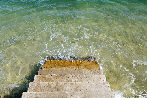 Concrete stairs going to the sea and green and blue sea surface