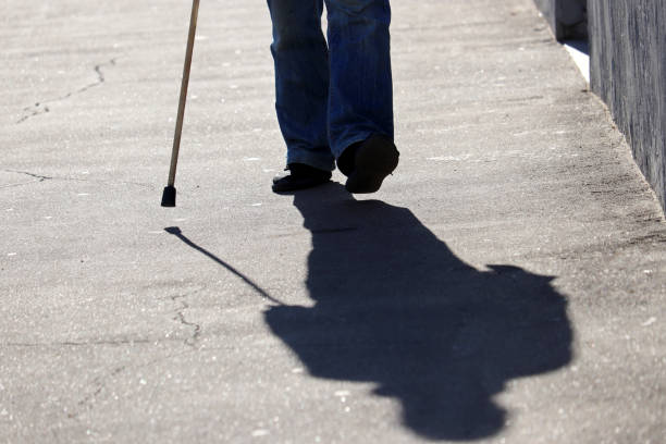 istock Man walking with a cane down the street, shadow on asphalt 1346120070