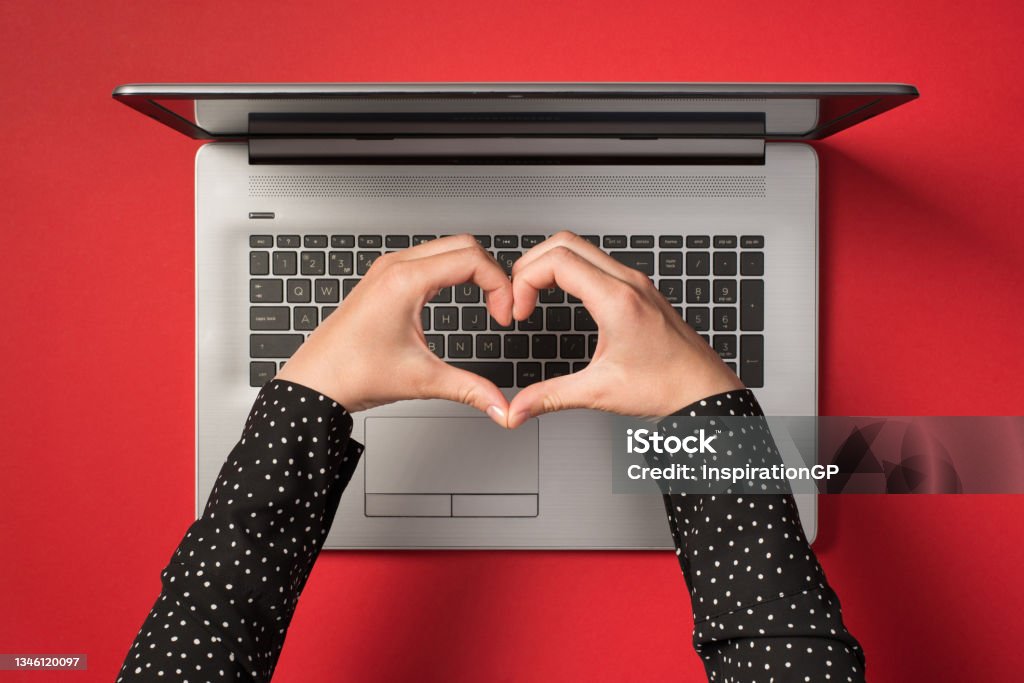 Overhead photo of grey laptop and hands with gesture as heart isolated on the red backdrop Love - Emotion Stock Photo