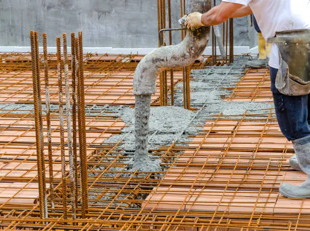 Construction worker pouring concrete into steel rebar frame