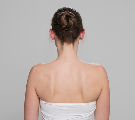 Rear view of mid adult woman with hair bun standing against gray background.