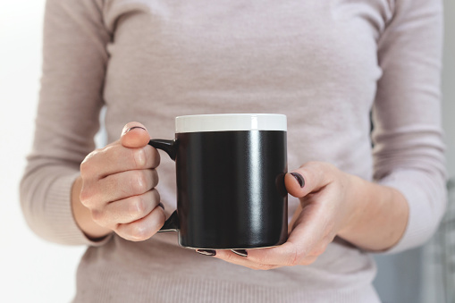 Black coffee mug mockup for design demonstration. Stylish cup mock up in female hands.