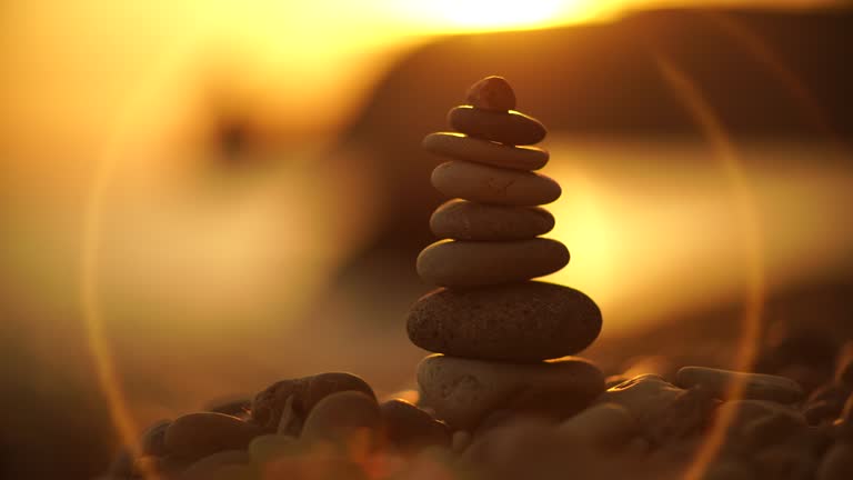 Balanced pebbles pyramid on the beach on sunny day and clear sky at sunset. Golden sea bokeh on background. Selective focus, zen stones on sea beach, meditation, spa, harmony, calm, balance concept