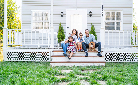 Happy family with two little children and pet dog siting on the steps of the porch