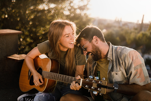 Happy woman playing a guitar to her boyfriend on a patio.
