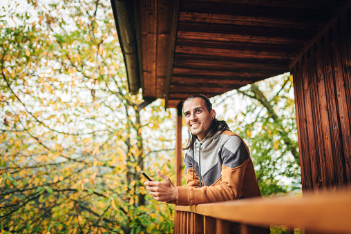 Fall is a beautiful season - young man enjoying the autumn view from a wooden terrace of a  lodge
