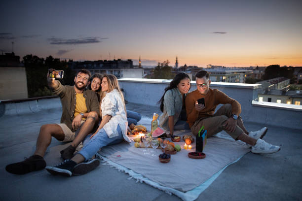 istock Young happy friends using cell phones during picnic evening on a roof. 1346124951