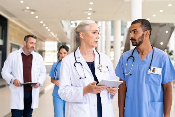 medico maturo e infermiere di razza mista che discutono il caso del paziente in ospedale - lab coat nurse doctor female doctor foto e immagini stock