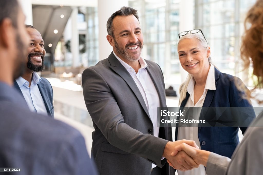 Business people shaking hands in meeting Happy mature businessman shaking hands with businesswoman in modern office. Successful entrepreneur greeting business woman with handshake. Agreement and business deal concept. Business Person Stock Photo