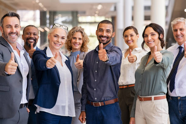 Group of successful business people showing thumbs up Group of happy multiethnic business people showing sign of success. Successful business team showing thumbs up and looking at camera. Portrait of smiling businessmen and businesswomen cheering at office. cheering group of people success looking at camera stock pictures, royalty-free photos & images