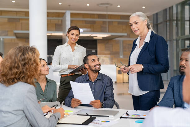 Multiethnic business team in meeting at modern board room Group of mixed race business people discussing work in conference room. Senior business manager guiding employees in meeting. Group of businessman and businesswoman working together while brainstorming and sharing new ideas and strategy. senior leadership meeting stock pictures, royalty-free photos & images