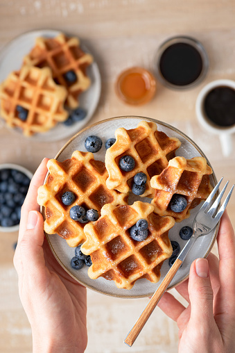 Waffles with blueberries in female hands, top view. Sweet food