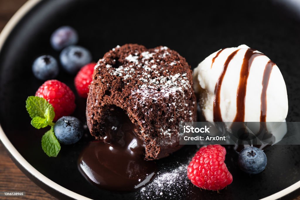 Chocolate fondant cake with ice cream scoop Chocolate fondant cake with berries and vanilla ice cream scoop on black plate, closeup view. Sweet dessert Chocolate Stock Photo