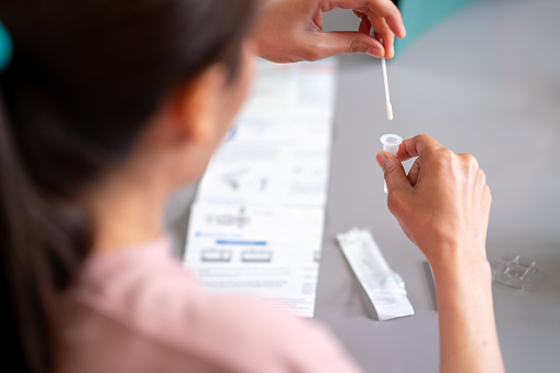 Mujer asiática que usa un kit de prueba rápida de antígenos para la autoevaluación de la epidemia de COVID-19 en casa. photo