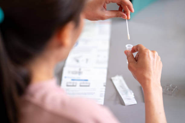 Asian woman using rapid antigen test kit for self test COVID-19 epidemic at home. Asian woman using rapid antigen test kit for self test COVID-19 epidemic at home. Adult female place the fabric tip of the swab in the extraction tube and rolling around the tube. COVID-19 pandemic protection concept. earbud stock pictures, royalty-free photos & images