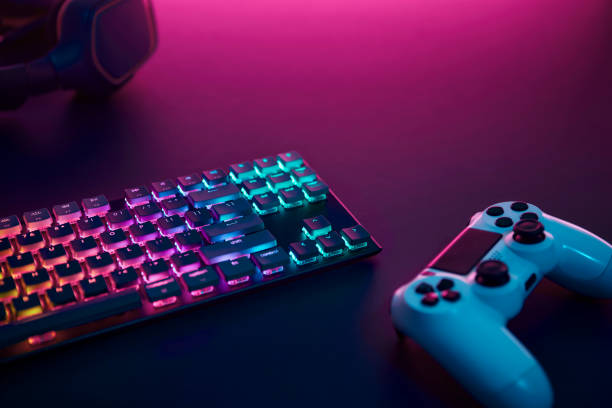 istock Rainbow color backlighted gaming keyboard, controller and stereo headphones. Purple light from top. 1346129679