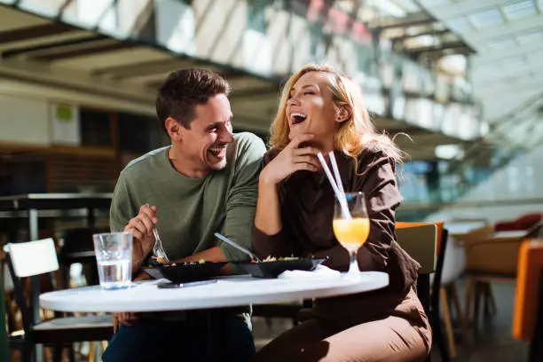 Happy young couple laughing while having lunch at a food court