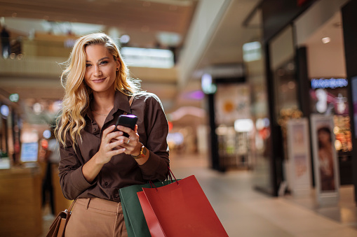 Portrait of beautiful blonde woman using smartphone in shopping mall