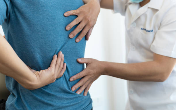 The doctor is diagnosing the patient's back pain. A male with back pain sees a doctor for treatment. stock photo