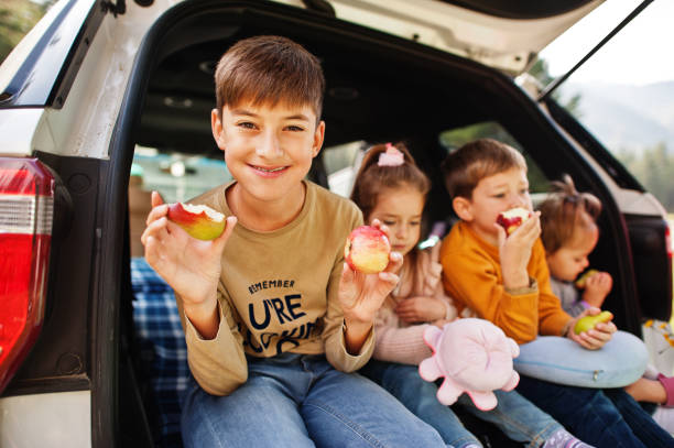 famiglia di quattro bambini mangia mele all'interno del veicolo. bambini seduti nel bagagliaio. viaggiare in auto in montagna, concetto di atmosfera. - 12 23 mesi foto e immagini stock