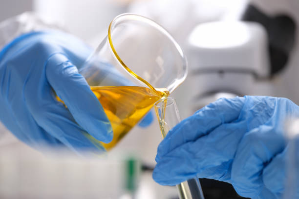 手袋をはめた科学者は、フラスコから黄色い油性液体を試験管に注ぎます。 - chemical agent ストックフォトと画像
