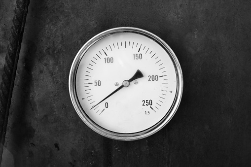 Axial thermometer mounted in rusty steel stove, close up vintage stylized black and white photo