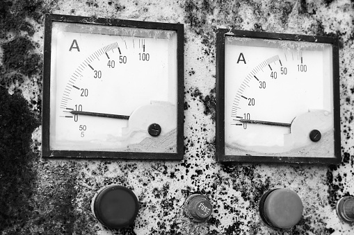 Two industrial square ammeters show zero power level, close up photo of a rusty old electric control panel. Vintage stylized black and white photo