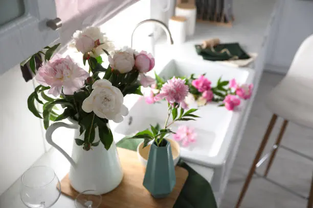 Beautiful peonies in vases on kitchen counter