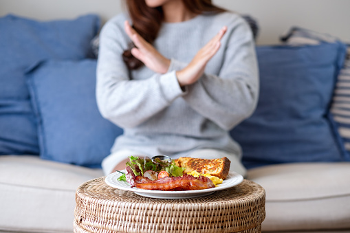 Una mujer haciendo una señal de mano con los brazos cruzados para rechazar la comida en la mesa photo