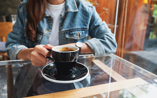 Closeup image of a woman holding and drinking coffee in cafe