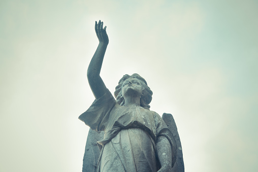 Angel with arm up, guiding the soul to heaven. Sculpture in a cemetery. Spiritual peace.