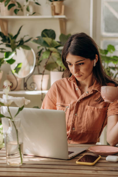 istock Young dark-haired mixed race woman using a laptop,drinking coffee at home.Cozy home interior with indoor plants.Remote work, business,freelance,online shopping,e-learning,urban jungle concept 1346143567
